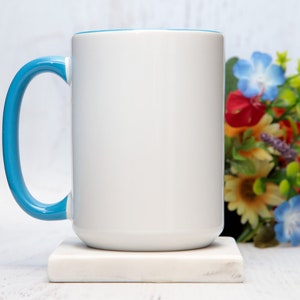 May include: A white ceramic mug with a light blue rim and handle. The mug is sitting on a white marble coaster.