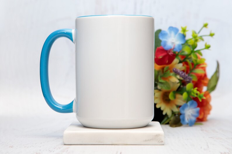 May include: A white ceramic mug with a light blue rim and handle. The mug is sitting on a white marble coaster.