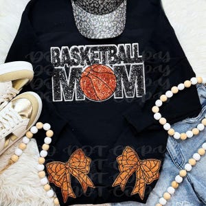 May include: Black sweatshirt with the text "Basketball Mom" in sparkly silver letters and a glittery orange basketball graphic. The sweatshirt has two orange glitter bows on the sleeves.