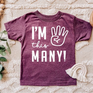 Może przedstawiać: Bordowy t-shirt z kr&oacute;tkim rękawem z białym napisem "I'm this many!" i białą ręką z uniesionymi czterema palcami.