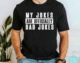 May include: A black t-shirt with white text that reads "My Jokes Are Officially Dad Jokes".