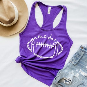 May include: Purple tank top with a white graphic of a football and the text "game day".