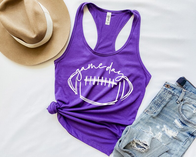 May include: Purple tank top with a white graphic of a football and the text "game day".