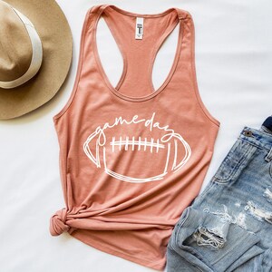 May include: A peach-colored tank top with a white graphic of a football and the text "game day".
