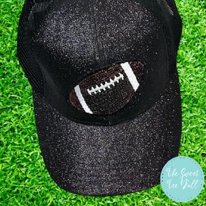 May include: A black baseball cap with a sparkly finish and a white and brown football design on the front. The cap has a mesh back.