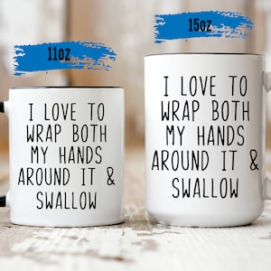 Pode incluir: Duas canecas de cerâmica branca com alças pretas. As canecas têm o texto "Eu adoro envolver ambas as mãos e engolir" impresso nelas. A caneca menor é de 11 oz e a caneca maior é de 15 oz.