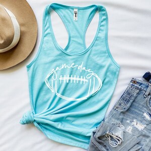 May include: A light blue tank top with a white graphic of a football and the text "game day".