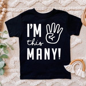 Może przedstawiać: Czarny T-shirt z białym tekstem "I'm this many!" i białą ręką z czterema uniesionymi palcami.