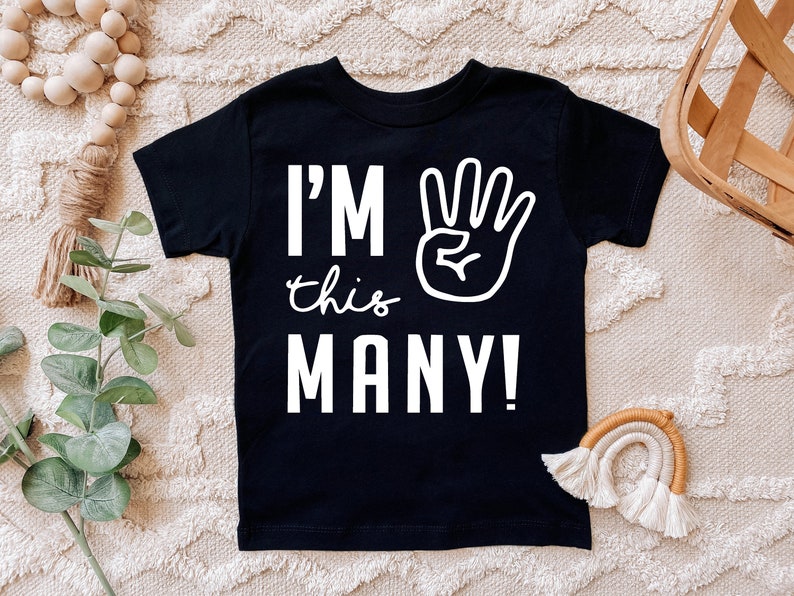 Może przedstawiać: Czarny T-shirt z białym tekstem "I'm this many!" i białą ręką z czterema uniesionymi palcami.