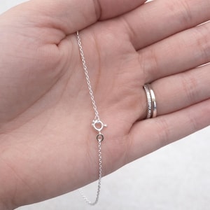 May include: A delicate silver necklace with a small clasp. The chain is thin and appears to be made of sterling silver. The necklace is shown against a light background.