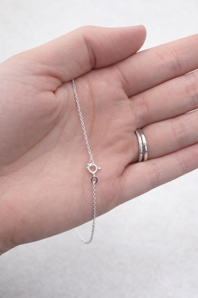 May include: A delicate silver necklace with a small clasp. The chain is thin and appears to be made of sterling silver. The necklace is shown against a light background.