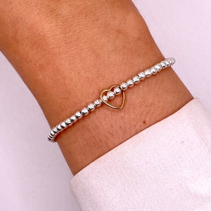 May include: A silver beaded bracelet with a gold heart charm.