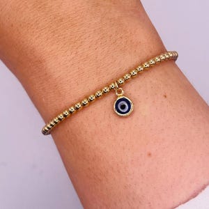 May include: A gold beaded bracelet with a blue and white evil eye charm.