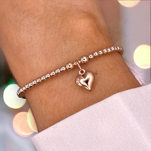 May include: A rose gold beaded bracelet with a heart charm. The bracelet is made of small, round beads and has a delicate, feminine look.
