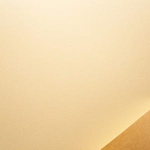 Puede incluir: Una superficie de papel lisa de color crema claro que ocupa la mayor parte del encuadre, con una esquina de un papel más oscuro y texturizado de color tostado visible en la sección inferior derecha, creando contraste entre los tonos.