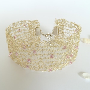 May include: A gold wire bracelet with a delicate crocheted design and pink beads.