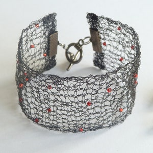May include: A black wire mesh bracelet with red beads. The bracelet has a clasp closure.