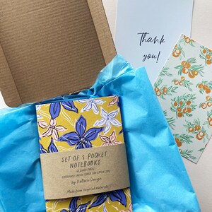 May include: Set of two pocket notebooks with floral designs on the covers. The notebooks are lined and have a patterned inside cover. The notebooks are made from recycled materials. The text on the cover reads "Set of 2 Pocket Notebooks 43 Lined Pages Patterned Inside Cover for Extra Joy by Kattern Design Made from recycled materials".