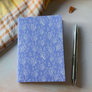 May include: A small, blue notebook with a white floral pattern. The notebook is closed and lying on a white surface.