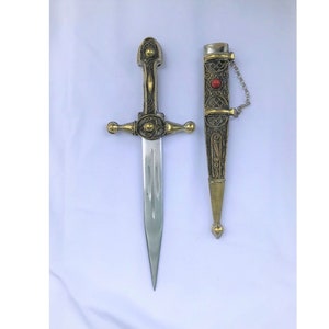 May include: A decorative dagger with a gold and silver finish. The dagger has a detailed design and a red jewel on the scabbard. The dagger is approximately 10 inches long.