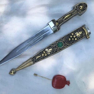 以下が含まれることがあります： 金と黒のハンドルと緑色の宝石が付いた装飾的な短剣。短剣は、金と黒のフィリグリーと緑色の宝石が付いたマッチングシースに入っています。