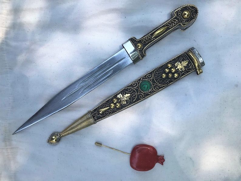 以下が含まれることがあります： 金と黒のハンドルと緑色の宝石が付いた装飾的な短剣。短剣は、金と黒のフィリグリーと緑色の宝石が付いたマッチングシースに入っています。