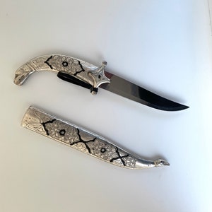 May include: A silver and black decorative knife with an ornate handle and a matching sheath.