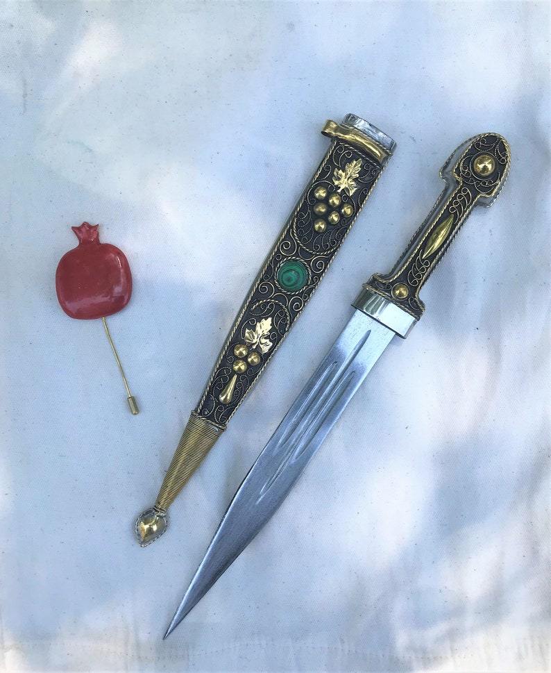 以下が含まれることがあります： 緑色の宝石と複雑な花の模様が施された、金と黒の鞘を持つ装飾的な短剣。短剣は銀の刃と金の柄を持っている。
