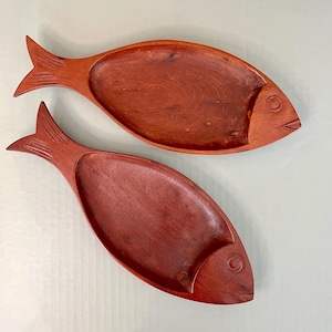 May include: Two wooden fish-shaped serving dishes. The dishes are a deep reddish-brown color and have a carved fish design.