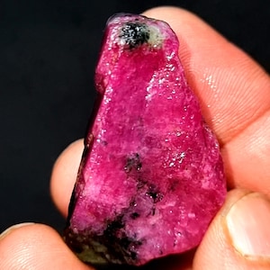 以下が含まれることがあります： 黒いインクルージョンが入った、大きな粗いピンクのルビーの宝石。ルビーは濃いピンク色で、光沢のある仕上がりです。