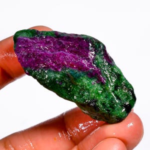 Puede incluir: Una gema en bruto con una vibrante combinación de colores. La piedra presenta un centro magenta intenso, rodeado por una banda verde, creando un contraste llamativo. La superficie tiene un aspecto natural y texturizado.