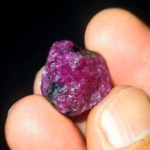 May include: A deep pink ruby gemstone with a rough, natural surface. The ruby is a vibrant, rich colour and has a slightly irregular shape.