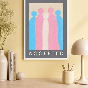 May include: A framed wall art print featuring a pointillist illustration of five abstract figures in blue, pink, and white. The figures are arranged side-by-side against a textured beige background. The word ACCEPTED is printed in white capital letters.