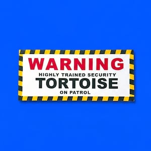 May include: A rectangular sign with a white background and a black and yellow striped border. The text reads WARNING in red, followed by HIGHLY TRAINED SECURITY TORTOISE ON PATROL in black, all in a bold, sans-serif font style.