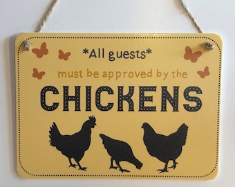 May include: A yellow sign with black text that reads "*All guests* must be approved by the CHICKENS". The sign has a string for hanging and features three black silhouettes of chickens. There are also brown butterfly silhouettes on the sign.