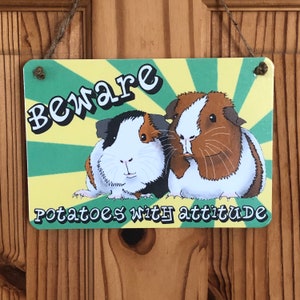 May include: A yellow and green sign with the text "Beware Potatoes with attitude" and a cartoon image of two guinea pigs.