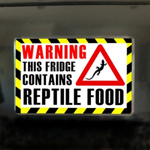 May include: A rectangular fridge magnet with a warning label. The label reads "WARNING THIS FRIDGE CONTAINS REPTILE FOOD" in black text. A red triangle with a lizard silhouette is on the right, with a yellow and black border.