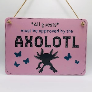 Peut inclure: Une pancarte en bois rose avec le texte "*All guests* must be approved by the AXOLOTL" en lettres noires. Une silhouette noire d'axolotl se trouve au centre de la pancarte avec des silhouettes de papillons bleus autour.