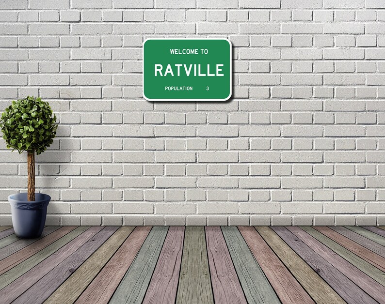 May include: A green road sign with white text that reads "Welcome to Ratville Population 3". The sign is mounted on a white brick wall. A small green bush is in a blue pot on the left side of the image.
