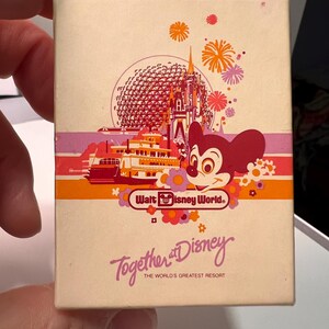 May include: A rectangular off-white box featuring a colorful graphic of Walt Disney World landmarks, including a castle, a geodesic dome, a riverboat, and Mickey Mouse. The text reads Walt Disney World, Together at Disney, and The World's Greatest Resort.
