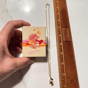 May include: A gold-tone chain necklace with a Mickey Mouse pendant, accompanied by a rectangular Walt Disney World box featuring a graphic of Spaceship Earth and the text Together at Disney. A brown ruler shows the necklace is 9 inches long.