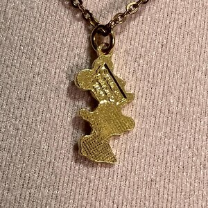 May include: A gold-toned metal pendant shaped like a cartoon mouse silhouette, suspended from a matching gold-toned link chain. The back of the pendant features embossed text that reads Disney and China, with a textured finish on the lower portion.