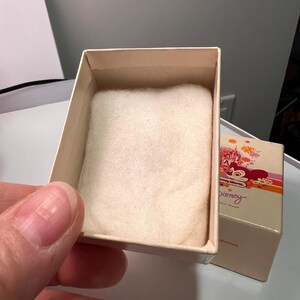 May include: A small, rectangular, cream-colored cardboard box with a soft, white, rectangular fabric insert inside. The box lid features a colorful graphic of a castle, fireworks, and the text Disney World and Disney.