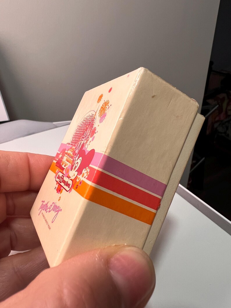 May include: A rectangular cream-colored box featuring a Walt Disney World logo, a graphic of Spaceship Earth, and a pink Minnie Mouse character. The box includes horizontal orange, red, and pink stripes and the text Together at Disney.