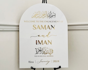 Pode incluir: Um sinal branco em forma de arco com letras douradas anunciando o noivado de Saman e Iman. O sinal inclui caligrafia árabe e a data "13th January 2024".