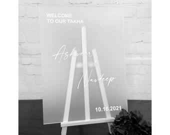 May include: White acrylic welcome sign with the text "Welcome to our Takha Ashveer & Navdeep 10.16.2021" on an easel.