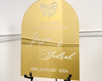 May include: Gold mirror welcome sign with an Arabic calligraphy heart design. The sign reads "Welcome to our beginning Yazan & Jedrah 24th January 2024".