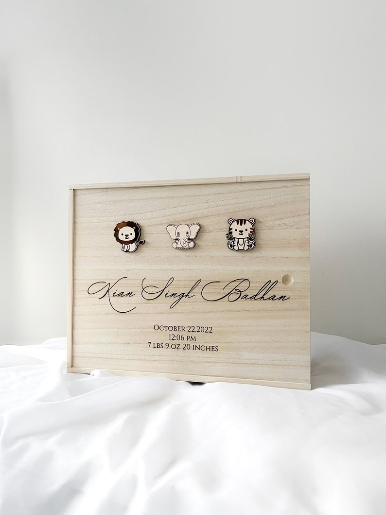 May include: A wooden keepsake box with a lion, elephant, and tiger design. The box is engraved with the name "Kian Singh Badhan", the date "October 22, 2022", the time "12:06 PM", and the baby's weight and length: "7 lbs 9 oz 20 inches".