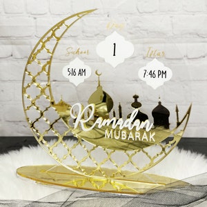 May include: Gold Ramadan countdown stand with a crescent moon design, featuring a day counter, Suhur and Iftar times, and the text "Ramadan Mubarak".