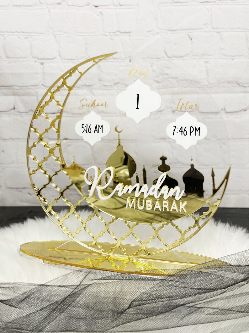 May include: Gold Ramadan countdown stand with a crescent moon design, featuring a day counter, Suhur and Iftar times, and the text "Ramadan Mubarak".